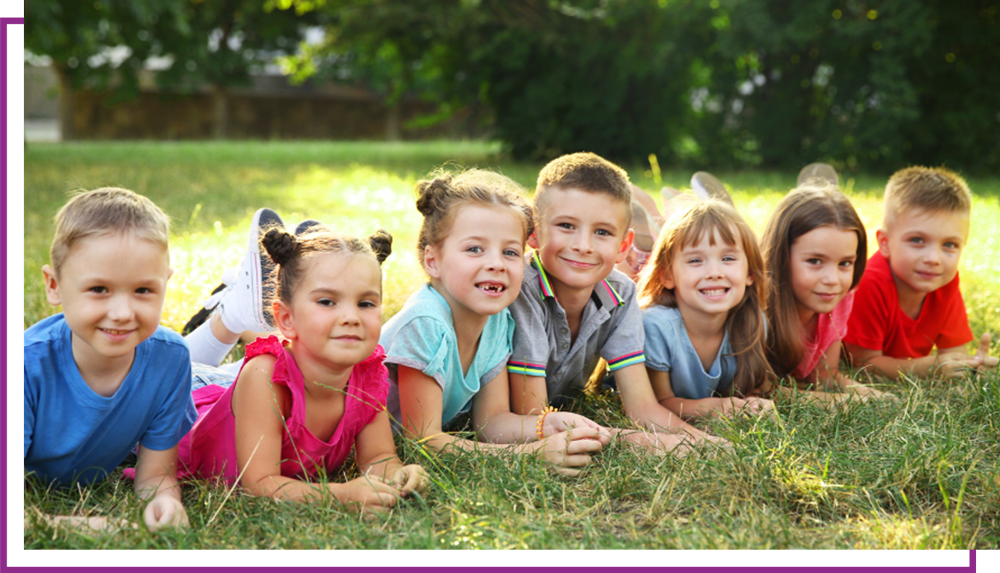 Children lying on grass outdoors, smiling at the camera in colorful shirts.