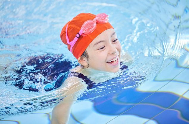 Smiling swimmer in orange cap and goggles in a blue pool