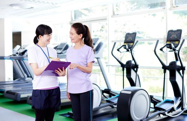 Two women talking in a bright gym beside treadmills and exercise bikes