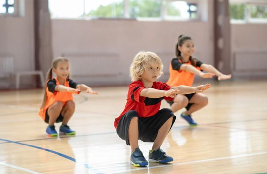 Children in orange vests doing squats in a gymnasium