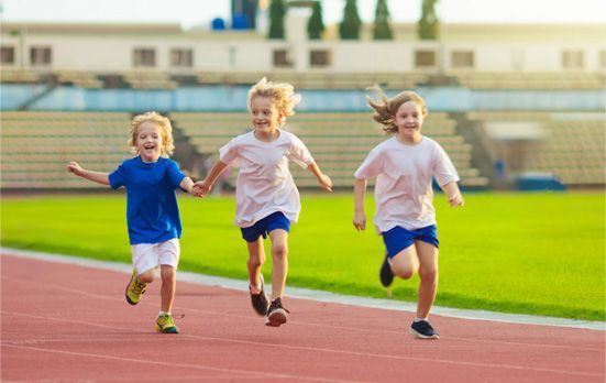 Three children running on a track at a stadium, smiling and wearing bright athletic clothes