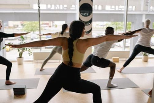 People practicing yoga in a bright studio, holding warrior poses on mats.