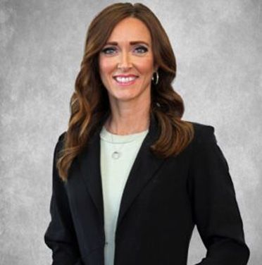 Woman in a black blazer and light top smiling against a gray studio backdrop