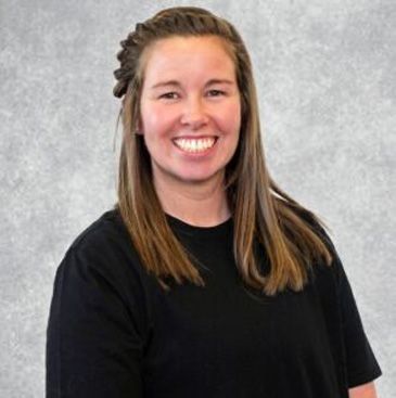 Smiling person in a black shirt standing against a gray backdrop.