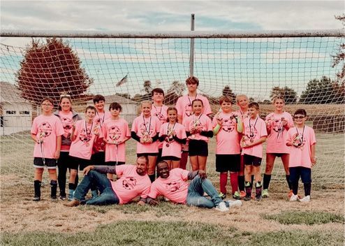 Youth soccer team in pink jerseys posing in front of a goal on a grassy field