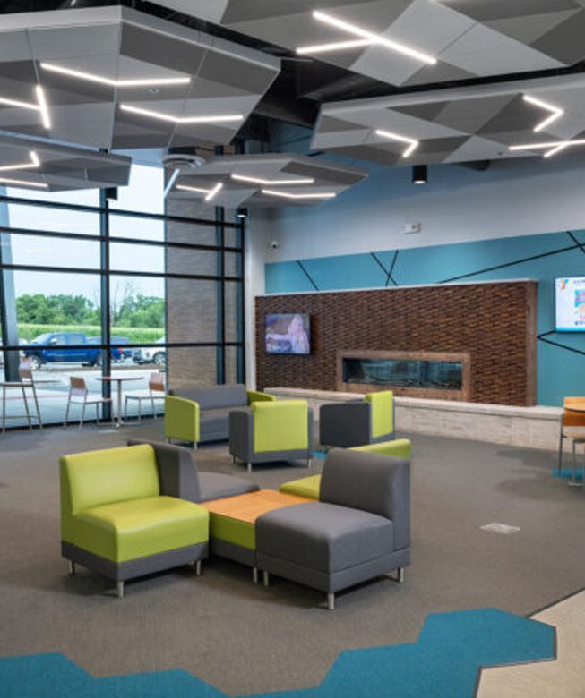 Modern lounge with lime and gray chairs, blue carpet accents, and a brick fireplace wall in a bright room
