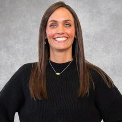 Smiling woman in a black sweater and necklace against a gray background