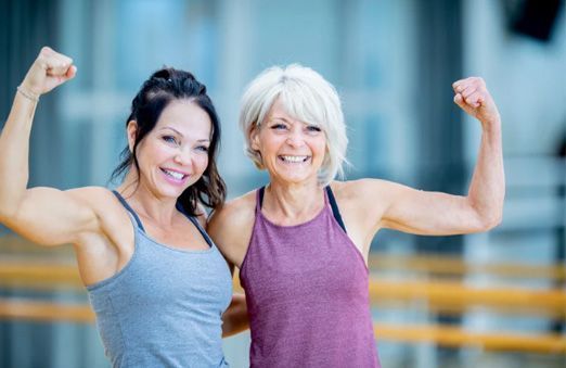 Two women flexing their arms and smiling in a gym-like setting