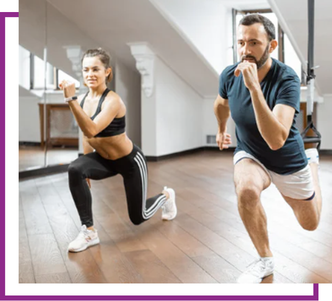 Two people doing lunges in a bright indoor workout space, one in black and one in blue and white shorts.