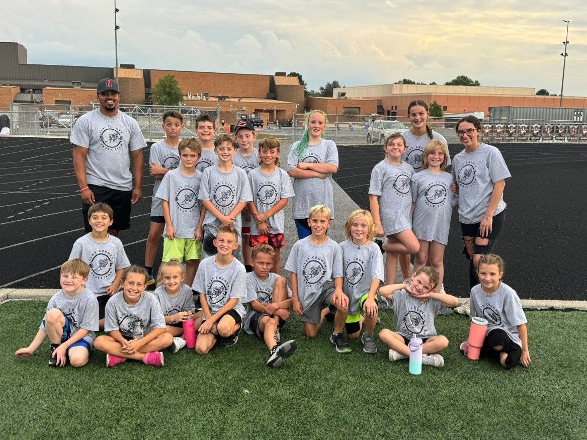 Youth sports team posing on a soccer field at sunset, wearing gray jerseys.