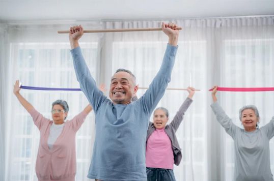 Group exercising with resistance bands in a bright studio, smiling and stretching arms overhead.