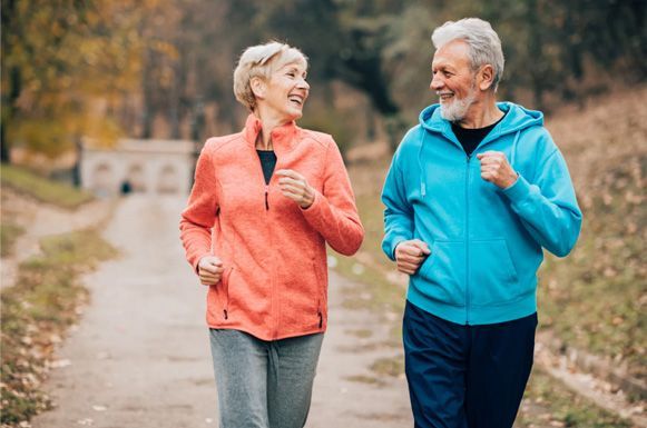 Two people jogging on a wooded path, smiling in colorful jackets.
