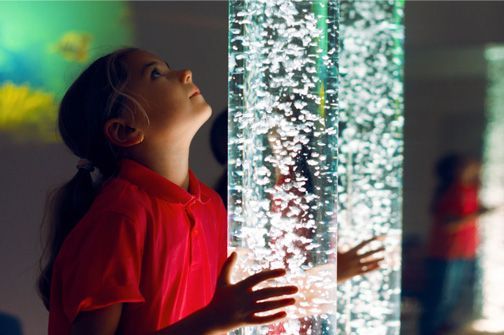 Girl in a red shirt gazing up at a glowing bubble wall in a colorful indoor exhibit