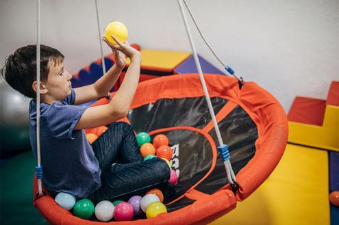 Child playing in an orange-and-black ball pit, holding yellow and blue balls with colorful balls around them