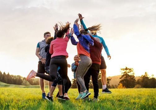 Group of people jumping and cheering together in a grassy field at sunset