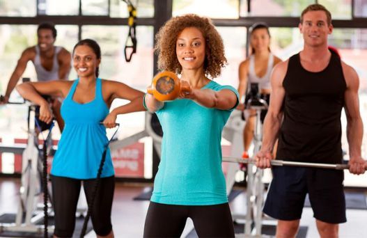 People exercising with dumbbells in a gym, led by a woman in a turquoise top