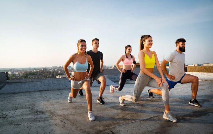 Group doing lunges on a rooftop at sunrise, wearing workout clothes.