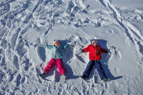 Two people lying in the snow making snow angels, one in pink pants and one in a red jacket