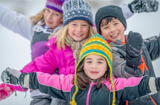 Children in colorful winter hats and jackets posing in the snow with arms outstretched