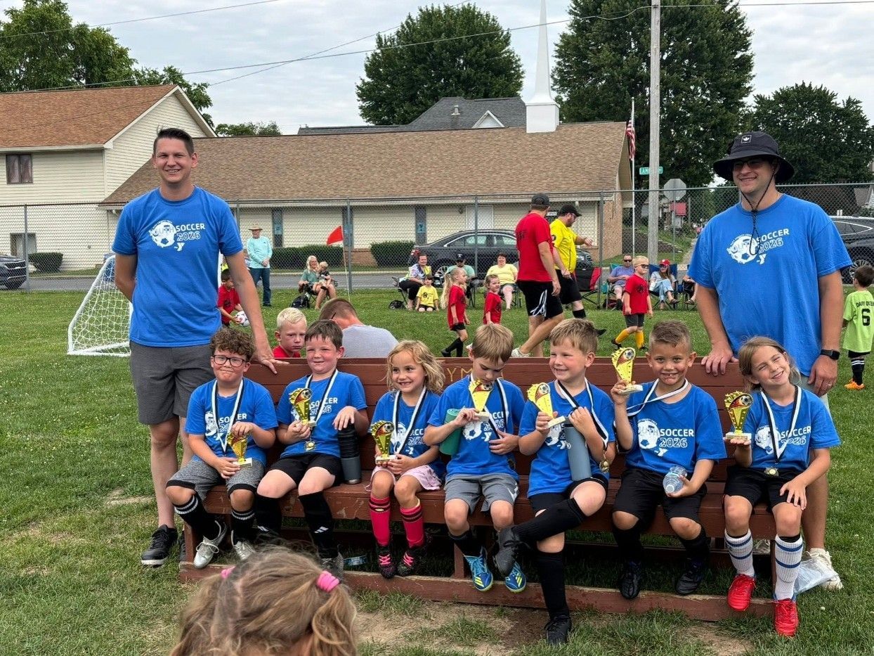 Youth soccer team posing with medals on a field, two coaches standing behind them.