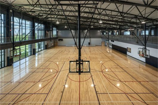 Empty indoor basketball court with polished wooden floor and tall glass windows