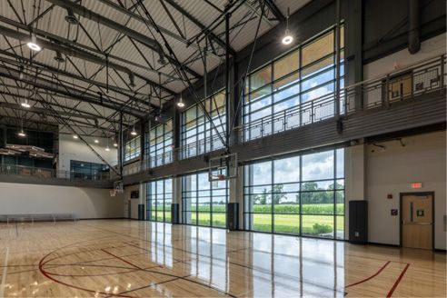 Empty indoor basketball court with high ceilings and large windows letting in daylight.
