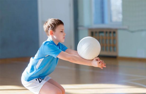 Volleyball player in blue jersey passing a white ball indoors on a gym court