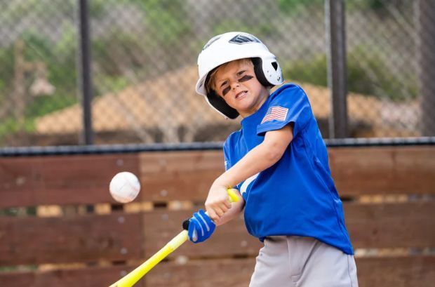 Young baseball player in blue swings a yellow bat at a ball on a field