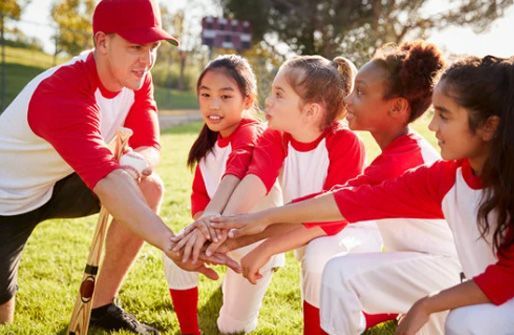 Coach and youth players stack hands during a soccer huddle on a sunny field