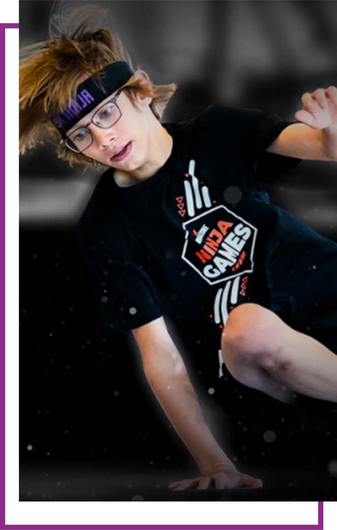 Person in glasses and headband posing mid-jump against a dark background.
