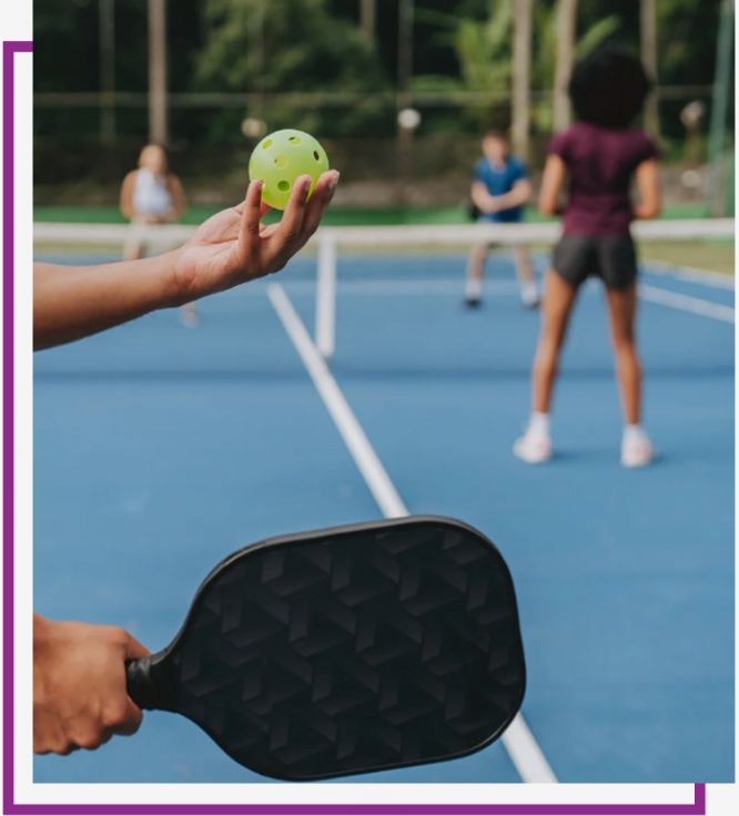 Pickleball players on a blue court, with a serve about to be hit in the foreground