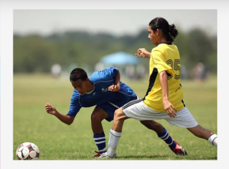 Two soccer players contesting the ball on a grassy field, one in blue and one in yellow