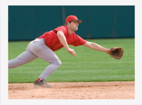 Baseball player in red uniform lunging low to field a ground ball on the infield dirt