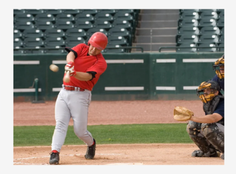 Baseball batter in red swings at home plate while catcher crouches behind him in a stadium.