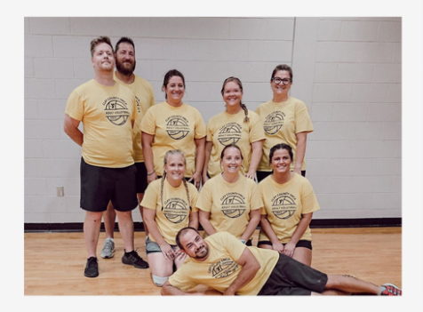 Group of people in yellow shirts posing in a gym, with one person lying across the front.