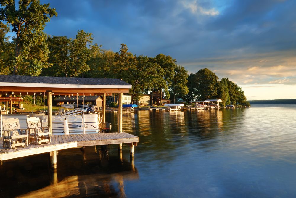 Wooden dock on a calm lake at dusk, with boats, trees, and cloudy sky.