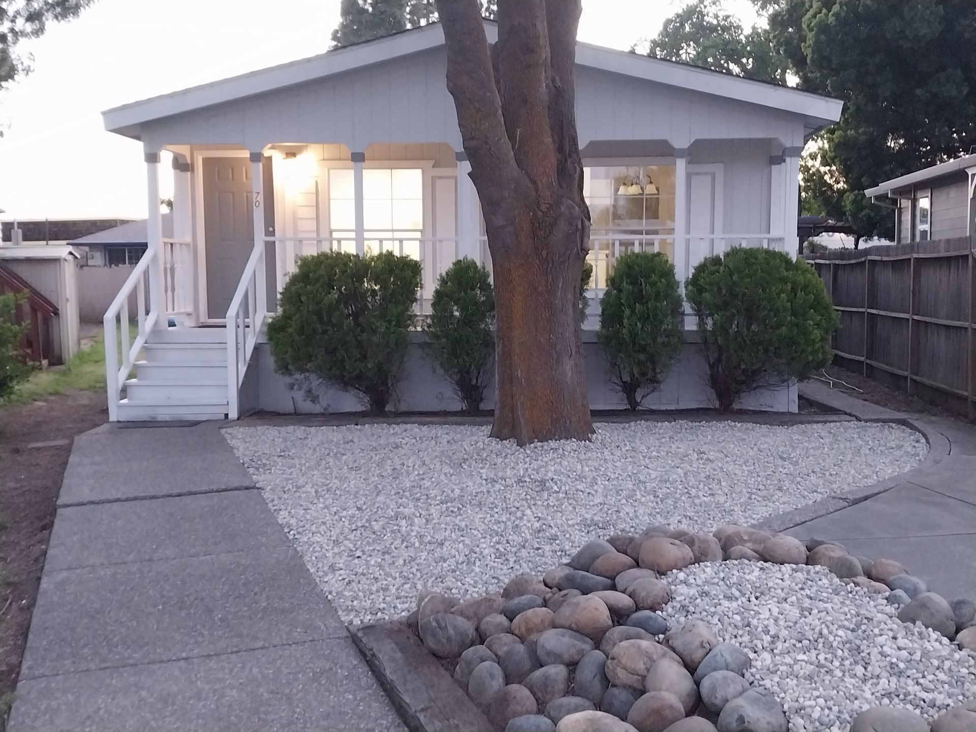 Small white house with front steps, gravel landscaping, and large rocks in the front yard.