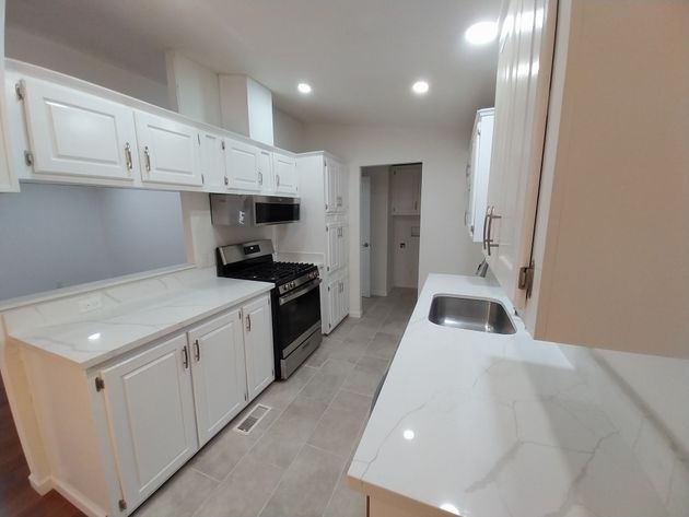 Bright white galley kitchen with cabinets, black stove, and marble-look countertops