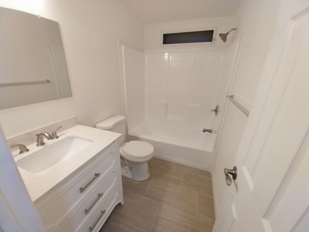 Small white bathroom with vanity, toilet, and shower tub, viewed from the doorway.