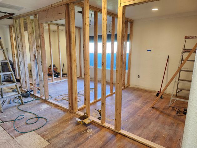 Interior under renovation with exposed wall studs, tools, and hardwood floors in a partially demolished room