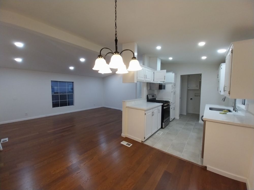 Open living room and kitchen with hardwood floors, white walls, and hanging pendant lights
