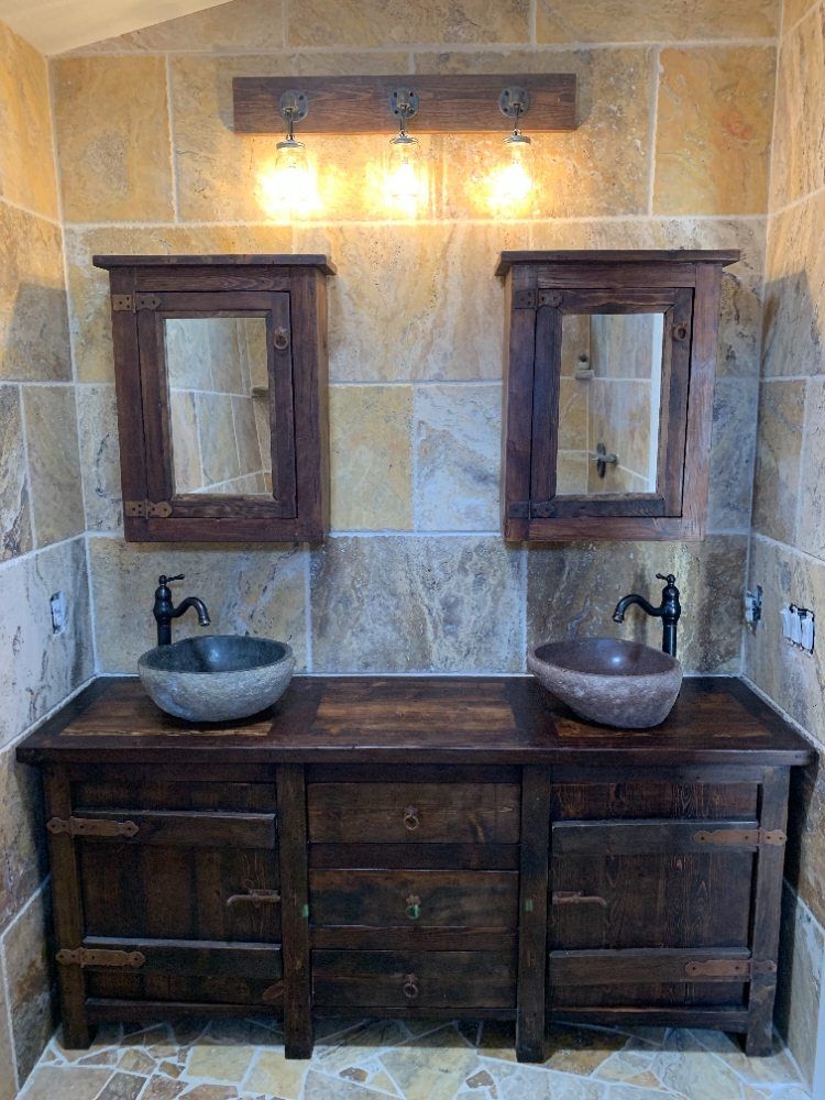 Rustic double vanity with stone sinks, wood cabinets, wall mirrors, and warm lights in a tiled bathroom