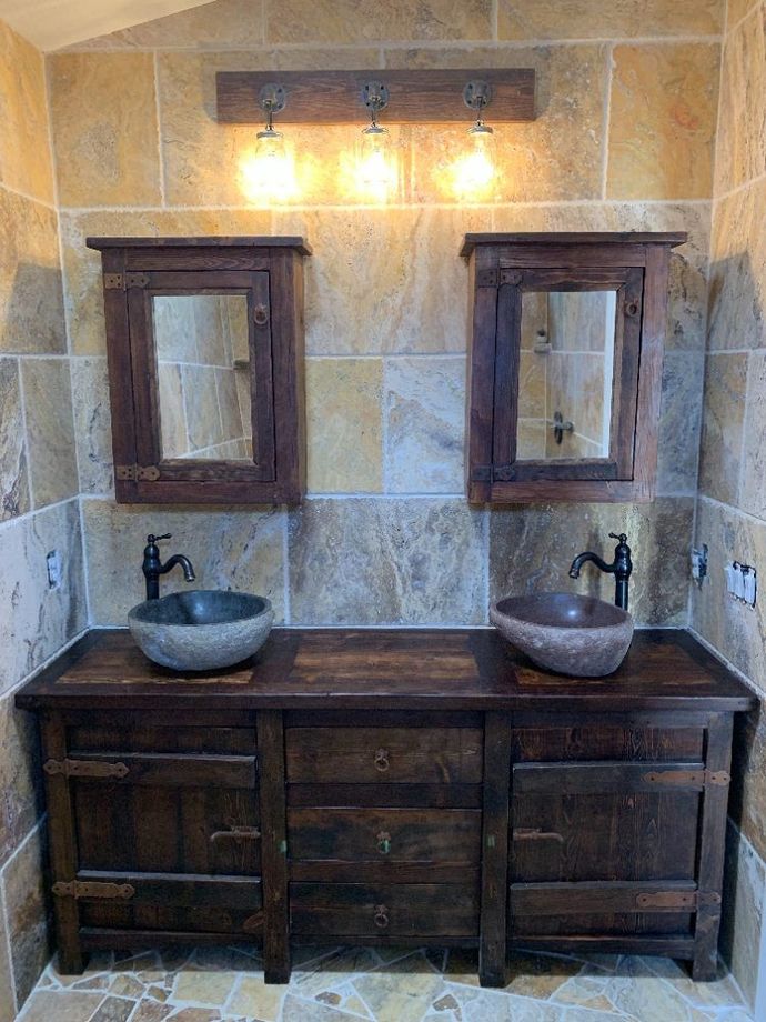 Rustic double vanity with stone sinks, wood cabinets, wall mirrors, and warm lights in a tiled bathroom
