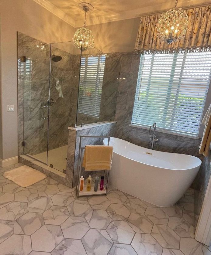 Modern bathroom with glass shower, freestanding tub, and mosaic tile floor under window blinds