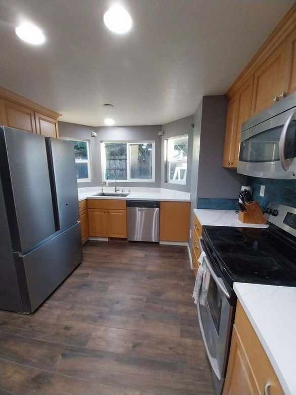 Bright modern kitchen with dark floor, wood cabinets, black appliances, and a window over the sink.