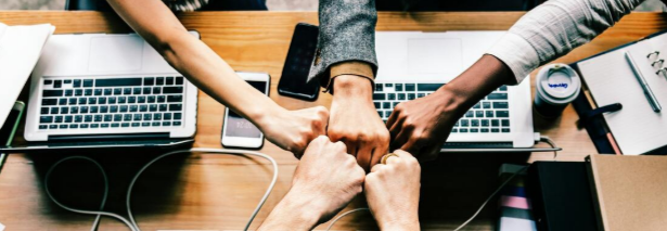 Picture of 5 people reaching over desks with computers putting there fists together in celebration