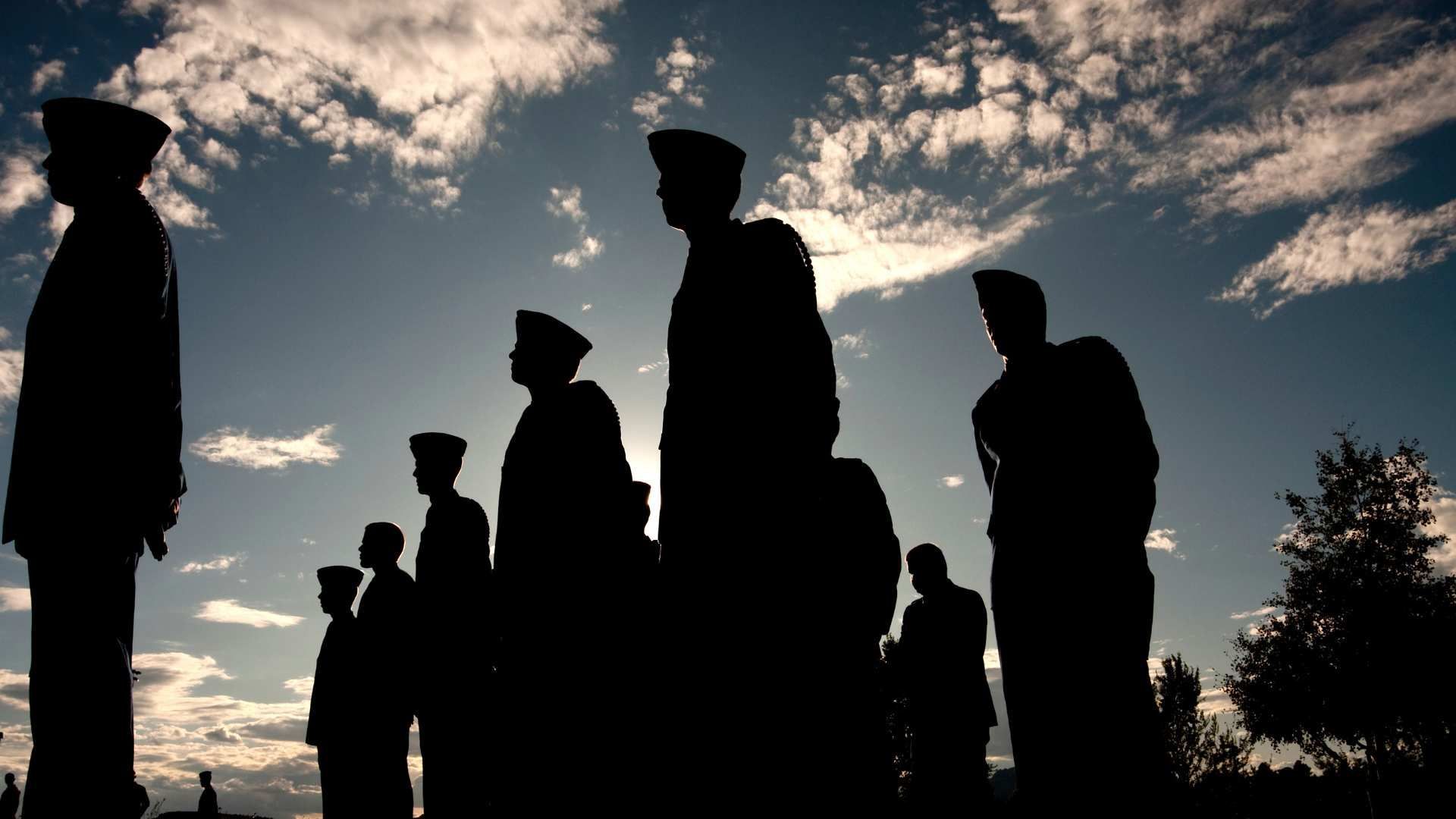 Silhouetted people standing outdoors at sunset under a cloudy sky