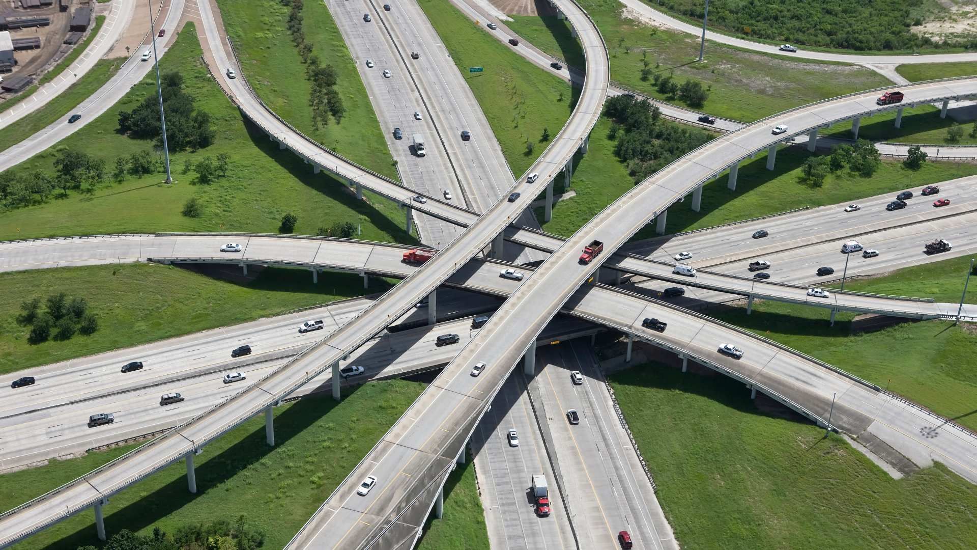 Aerial view of a multi-level highway interchange with cars crossing over green grassy medians.