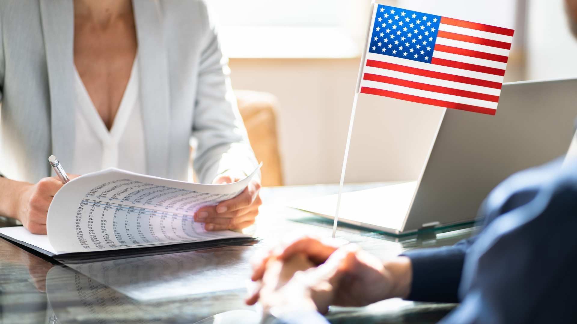 Two people in a bright office discuss paperwork beside a small U.S. flag on a desk