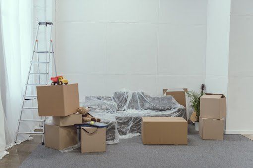 Cardboard boxes, sofa covered in plastic, and toys in a room, moving day.